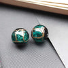 A pair of handcrafted lampwork glass beads with gold accents resting on a dark gray surface.