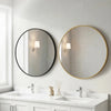 A round gold-framed wall mirror above a white vanity with marble countertop and modern faucets.