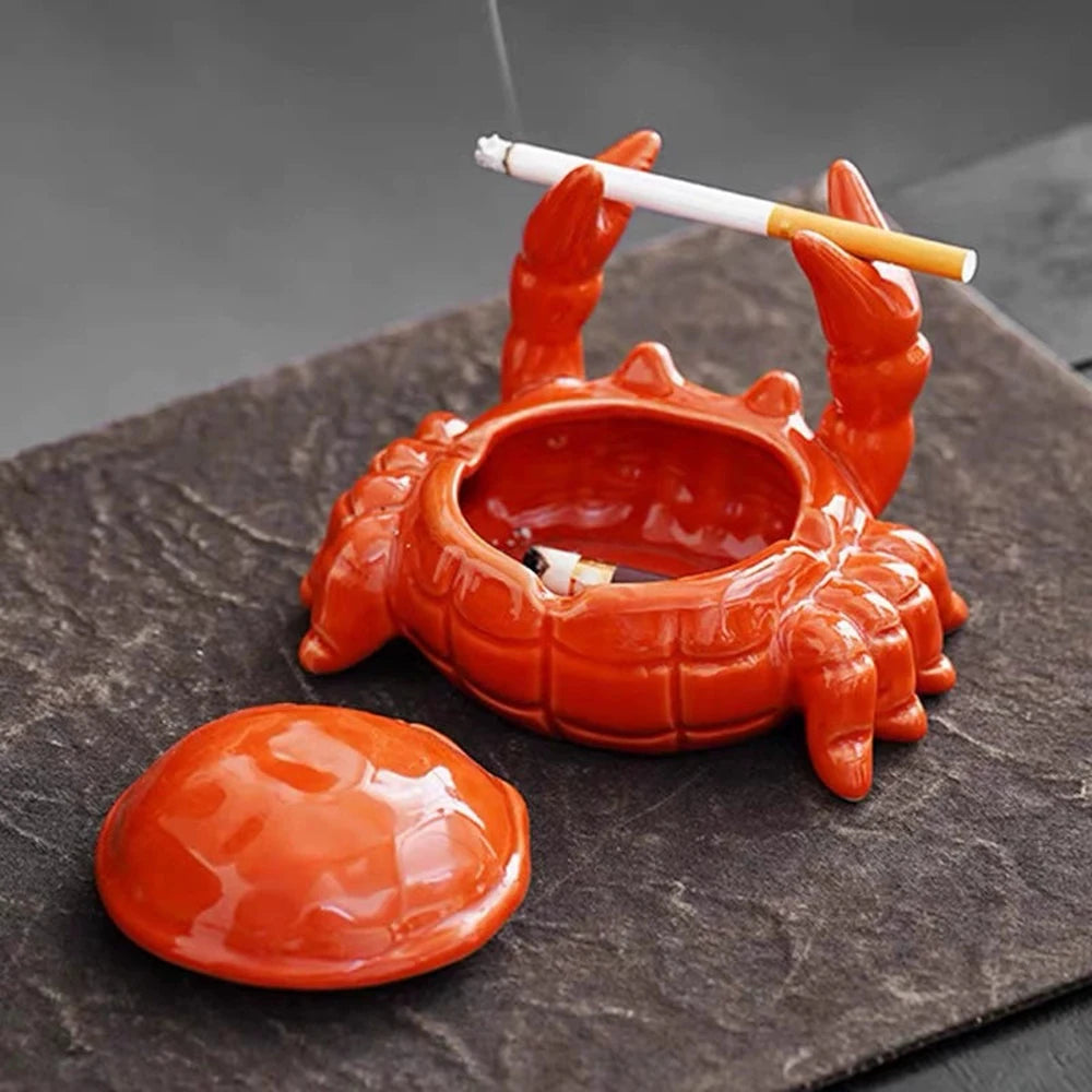 An orange ceramic crab ashtray with a lid resting on a dark slate surface.