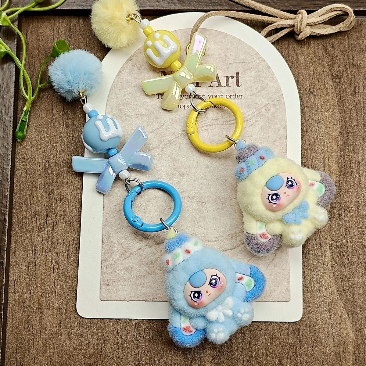 A set of cute heart plush keychain charms in blue and yellow, featuring a fluffy pom-pom and a stylized heart design.