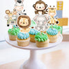 A display of jungle animal cake toppers featuring monkeys, elephants, and other animals on a white cake stand.