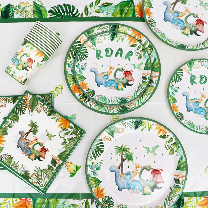 A green and white dinosaur party disposable tableware set with a banner and balloons displayed on a white surface.