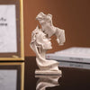 Une petite statue en résine de couleur claire représentant deux visages s'étreignant, présentée sur une surface réfléchissant