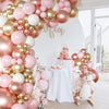 A pink and gold latex balloon garland decorated with roses and macarons for a celebration.