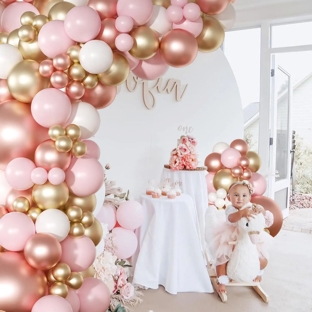 A pink and gold latex balloon garland decorated with roses and macarons for a celebration.