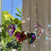 A collection of iridescent, heart-shaped glass pendants hanging against a bright window background.