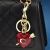 Colgante y llavero en forma de corazón dorado sujeto a un bolso de mano acolchado negro.