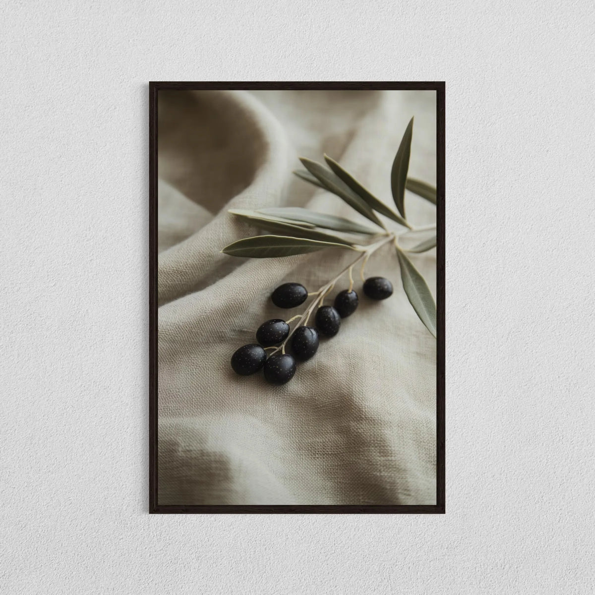 A close-up photograph of dark olives and olive leaves on a beige fabric, framed as wall art.