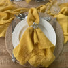 A stack of ten handcrafted fringed yellow cotton napkins tied with silver accents, displayed on a woven mat.