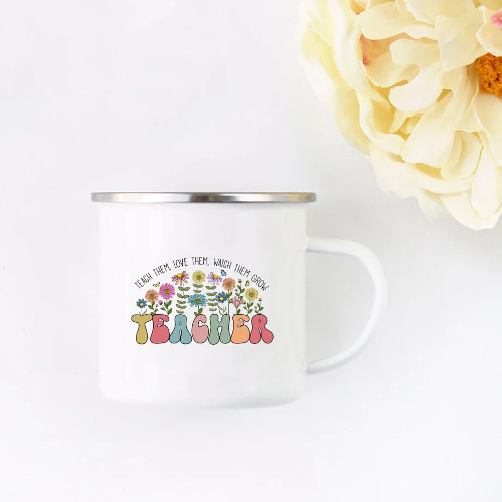 A white enamel mug with a floral design and the word TEACHER printed on it, set against a white background.