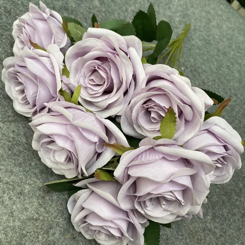 A bouquet of nine realistic silk roses in soft lavender and pale purple shades.
