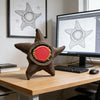 A brown, starfish-shaped fidget toy with an open center, resting on a wooden desk next to a computer monitor.