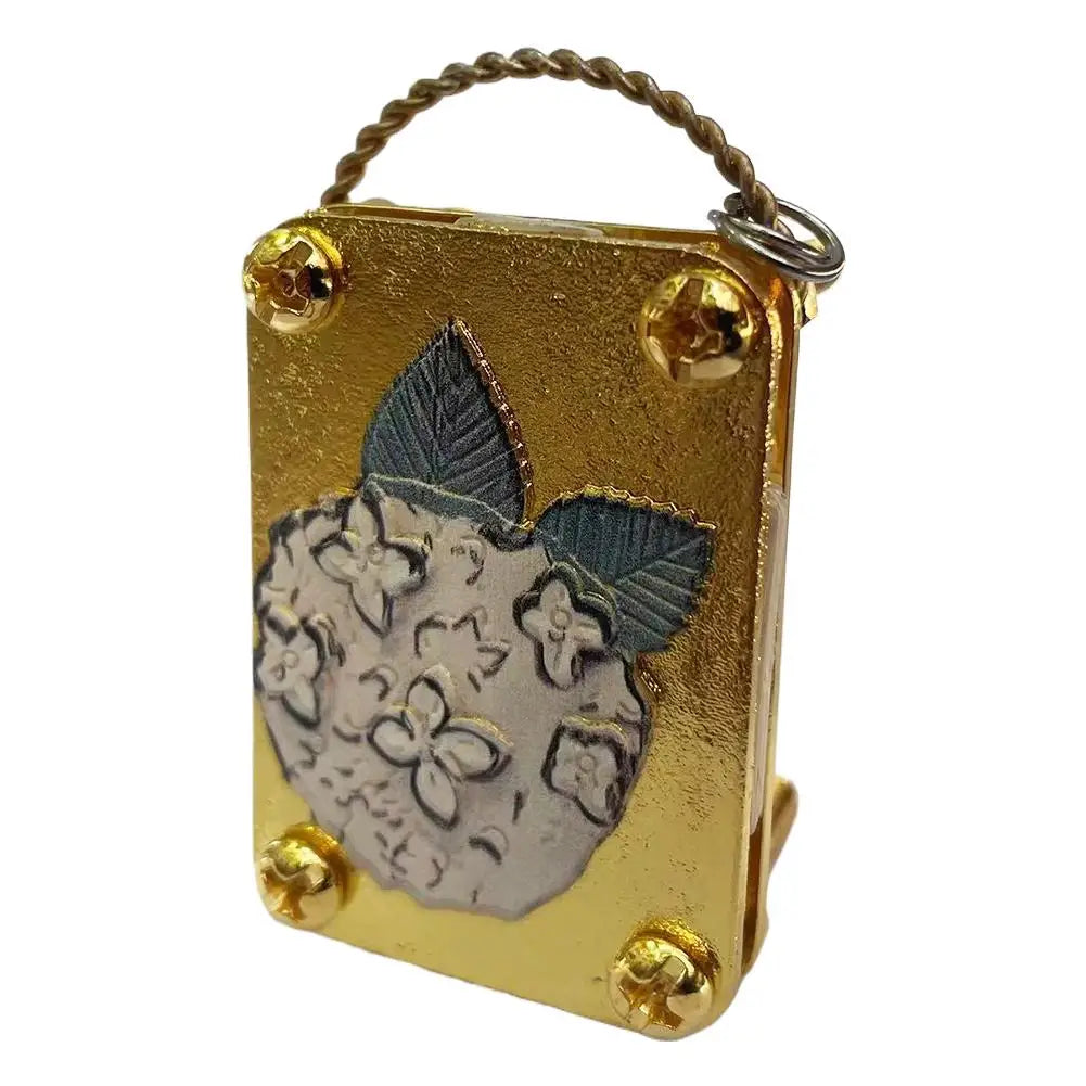A small, rectangular brass metal press kit with a wire loop handle and a pressed flower design on the surface.