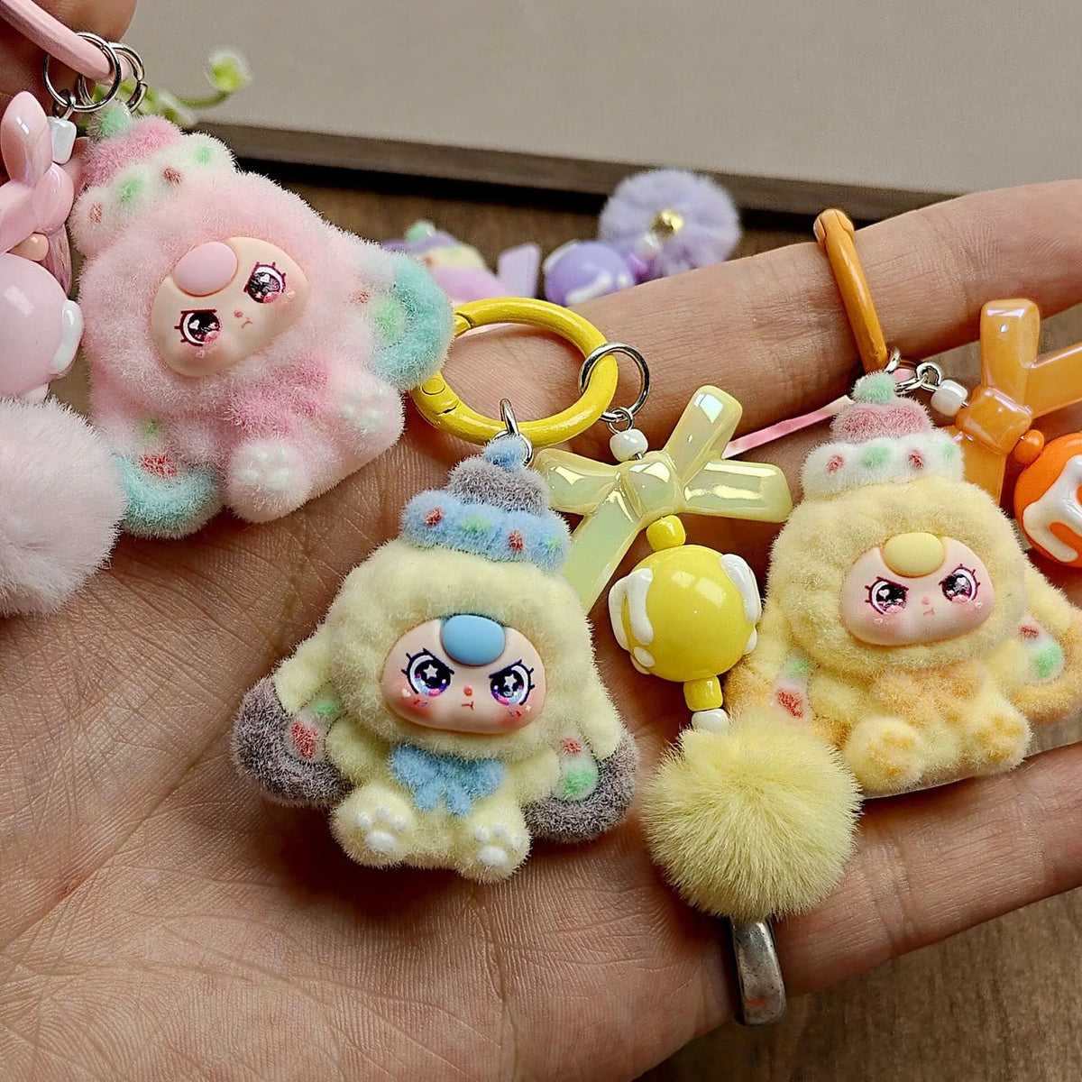 A hand holds several cute heart plush keychain charms in pastel colors like pink, yellow, and purple.