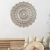 Decoración de pared tipo mandala de madera clara junto a un sombrero tejido y muebles de madera.