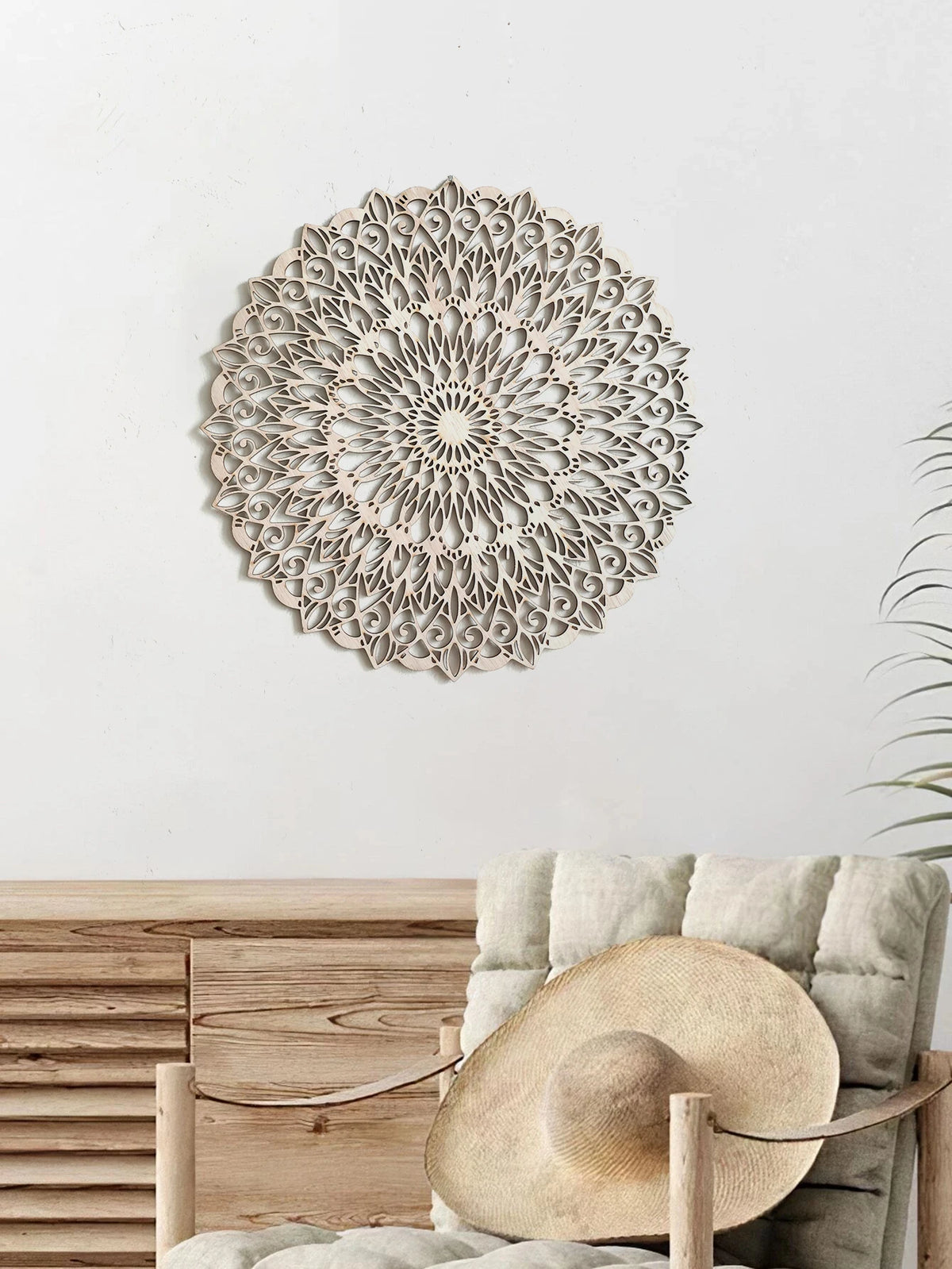 Decoración de pared tipo mandala de madera clara junto a un sombrero tejido y muebles de madera.
