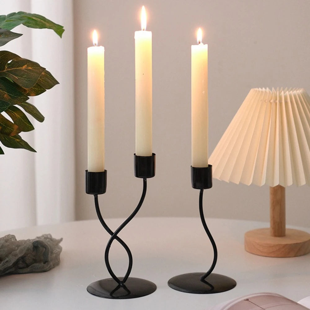 A set of three tall white candles in black iron holders on a white table.