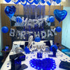 A blue and silver balloon decoration setup for a birthday party featuring heart shapes, foil letters, and blue confetti on a 
