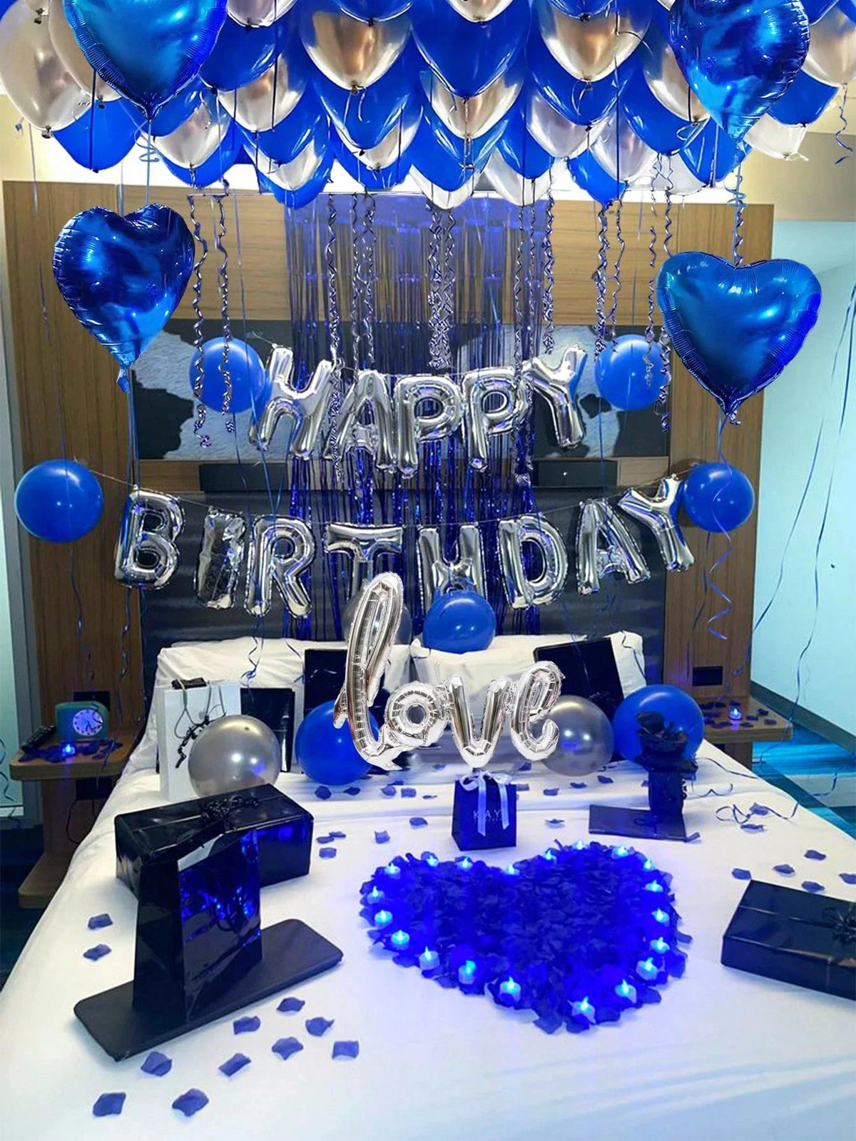 A blue and silver balloon decoration setup for a birthday party featuring heart shapes, foil letters, and blue confetti on a 
