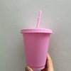A hand holds a pink plastic cold cup with a lid and straw against a light gray wall.