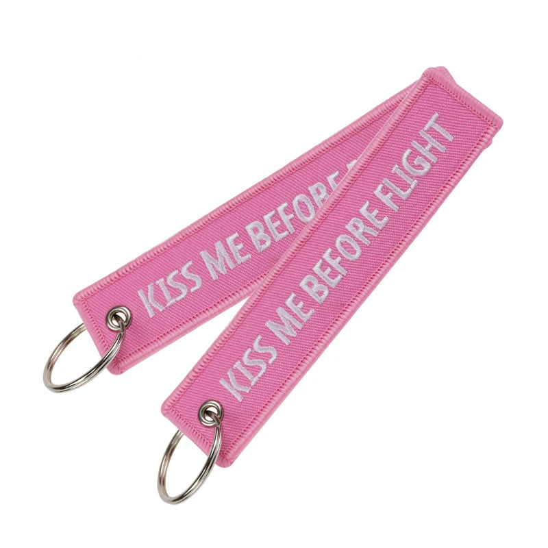 Pink woven keychain with the text Kiss Me Before Flight
