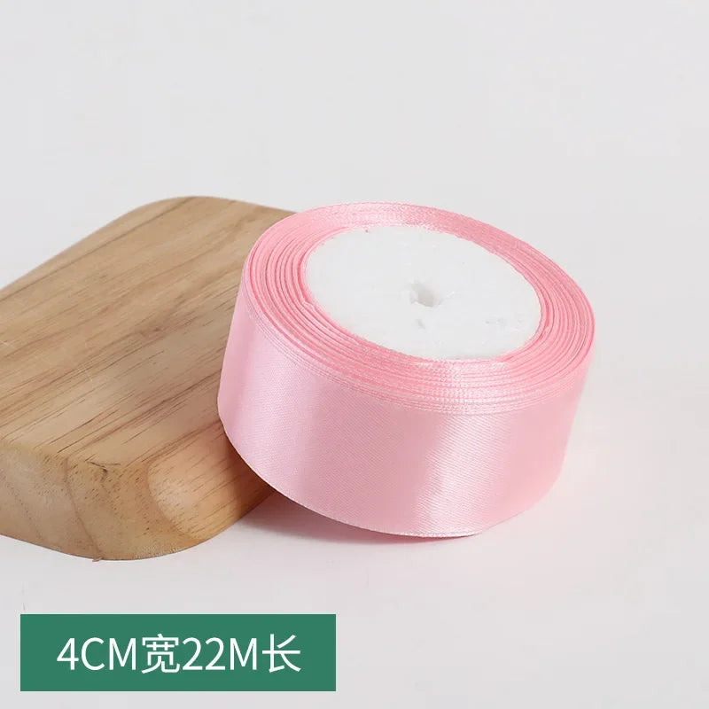 Roll of pink silk satin ribbon with a white center, shown next to a wooden block.