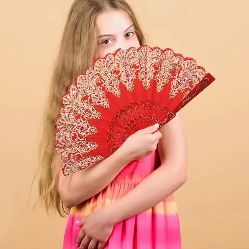 A girl holds a red and gold folding fan with traditional Chinese design.