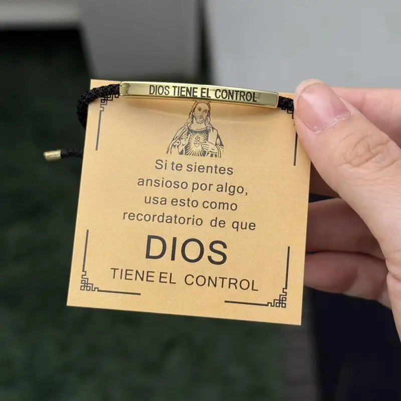 A close-up of a gold-toned stainless steel bracelet with an engraved tag featuring the text Dios Tiene El Control