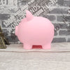 A pink piggy bank is sitting on a wooden surface against a brick wall background.