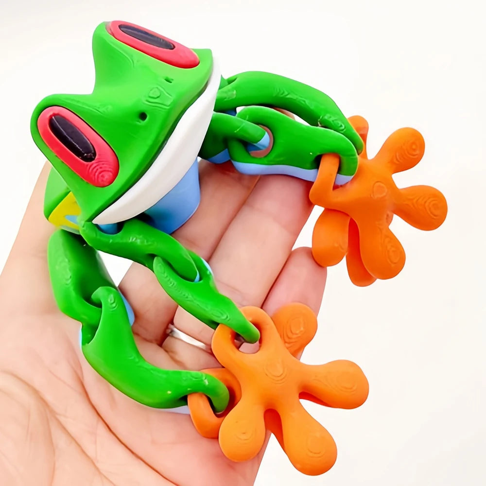 A realistic, movable 3D printed frog fridge magnet in green and orange colors being held in a hand.