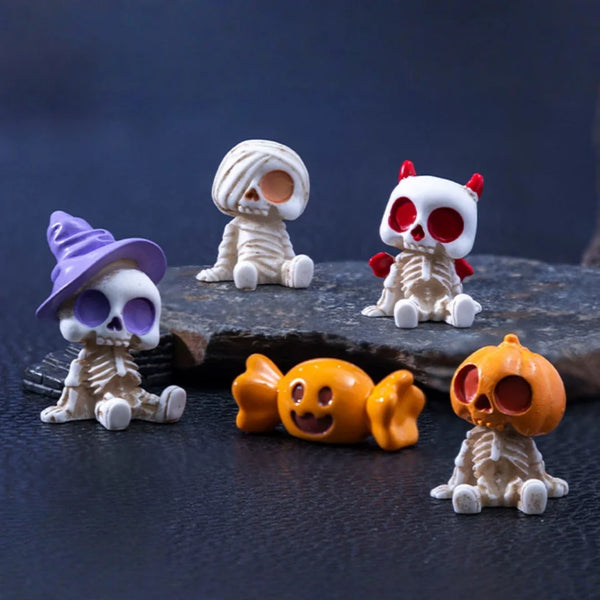 A set of spooky resin Halloween decor featuring skulls and a cat figurine on a dark surface.