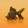 A small, detailed retro brass goldfish statue with textured scales, resting on a smooth orange surface.