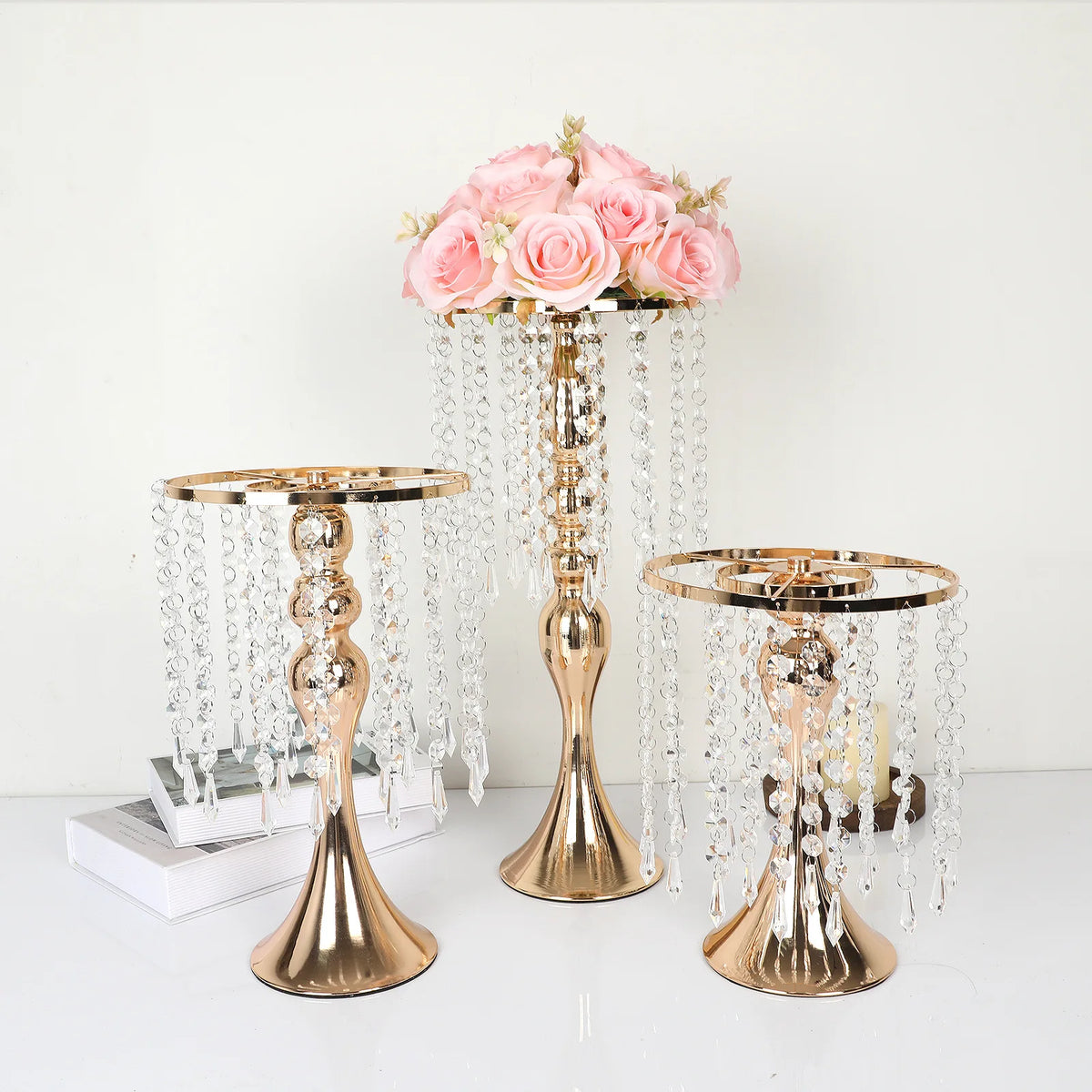 A gold crystal flower centerpiece stand with cascading crystal strands and pink roses.