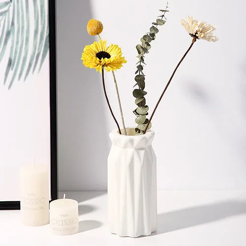 A white plastic vase holds a yellow flower and green foliage, set against a light background.