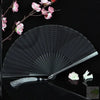 A black titanium alloy folding hand fan with a white tassel is displayed against a dark background.