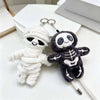A white mummy skeleton plush keychain with a black skeleton design and a silver chain.