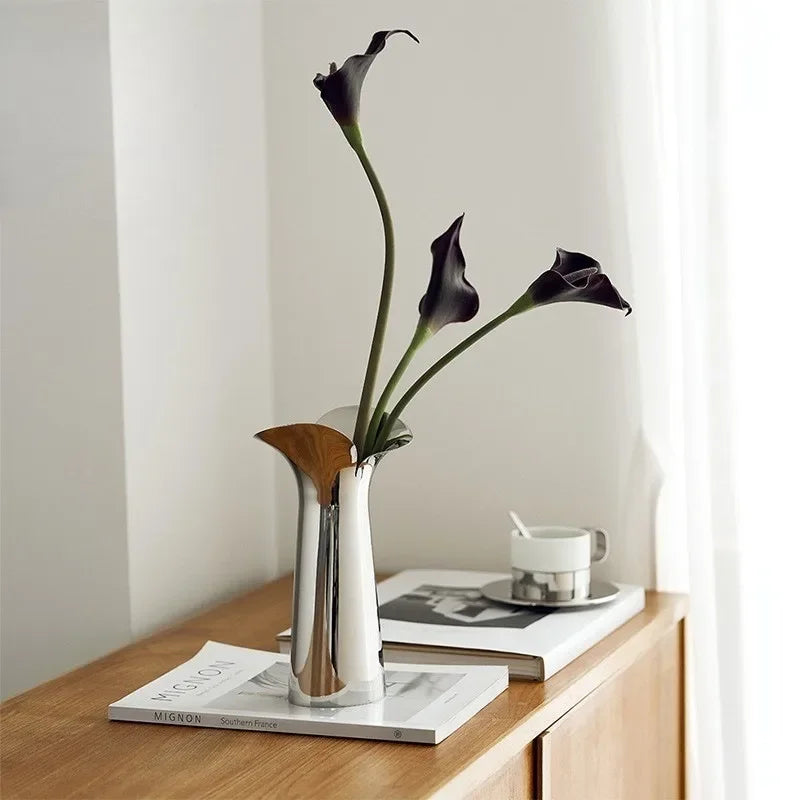 A silver-plated ceramic vase holds a stem of dark purple or black orchid flowers against a white background.