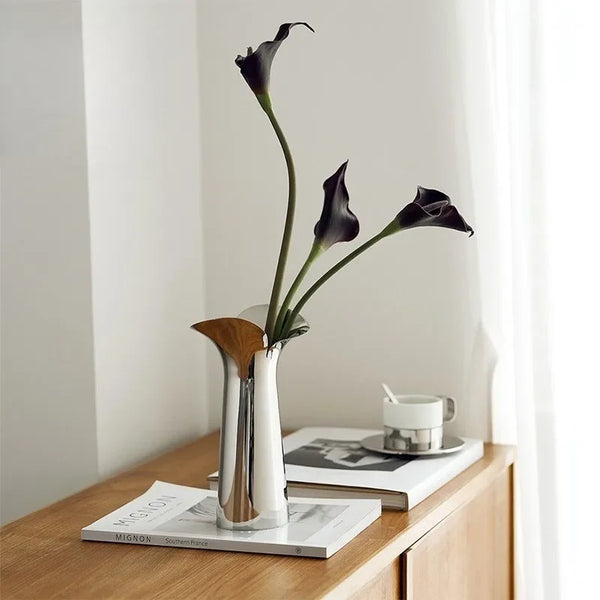 A silver-plated ceramic vase holds a stem of dark purple or black orchid flowers against a white background.