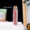 A glass bottle filled with pink red strawberry crystals sits on a white surface.