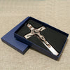 A silver crucifix with a figure of Christ inside, set in a dark blue velvet box for wall decor.