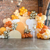 A vibrant balloon arch display featuring orange, gold, and silver latex balloons for a party or wedding decor.