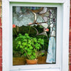 A decorative window decal shaped like a spider web with a small spider hanging in front of greenery.