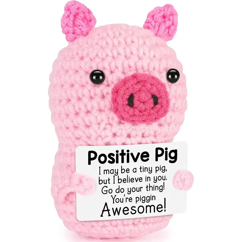 A pink crocheted pig toy with a positive message card attached.