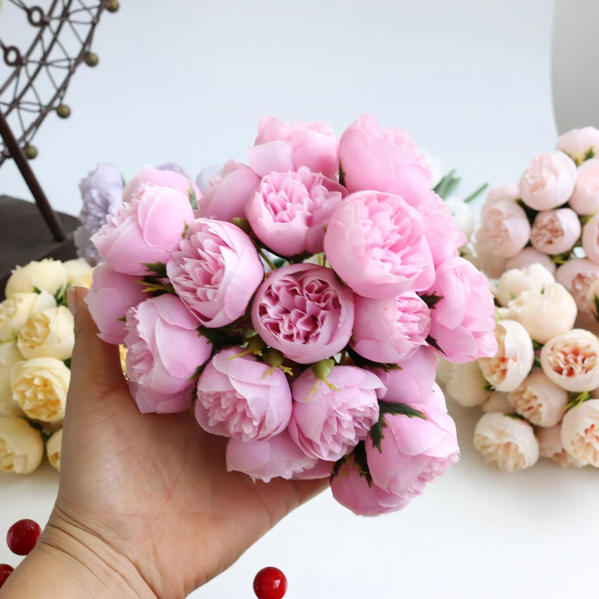 A hand holds a bouquet of artificial pink peony silk flowers.