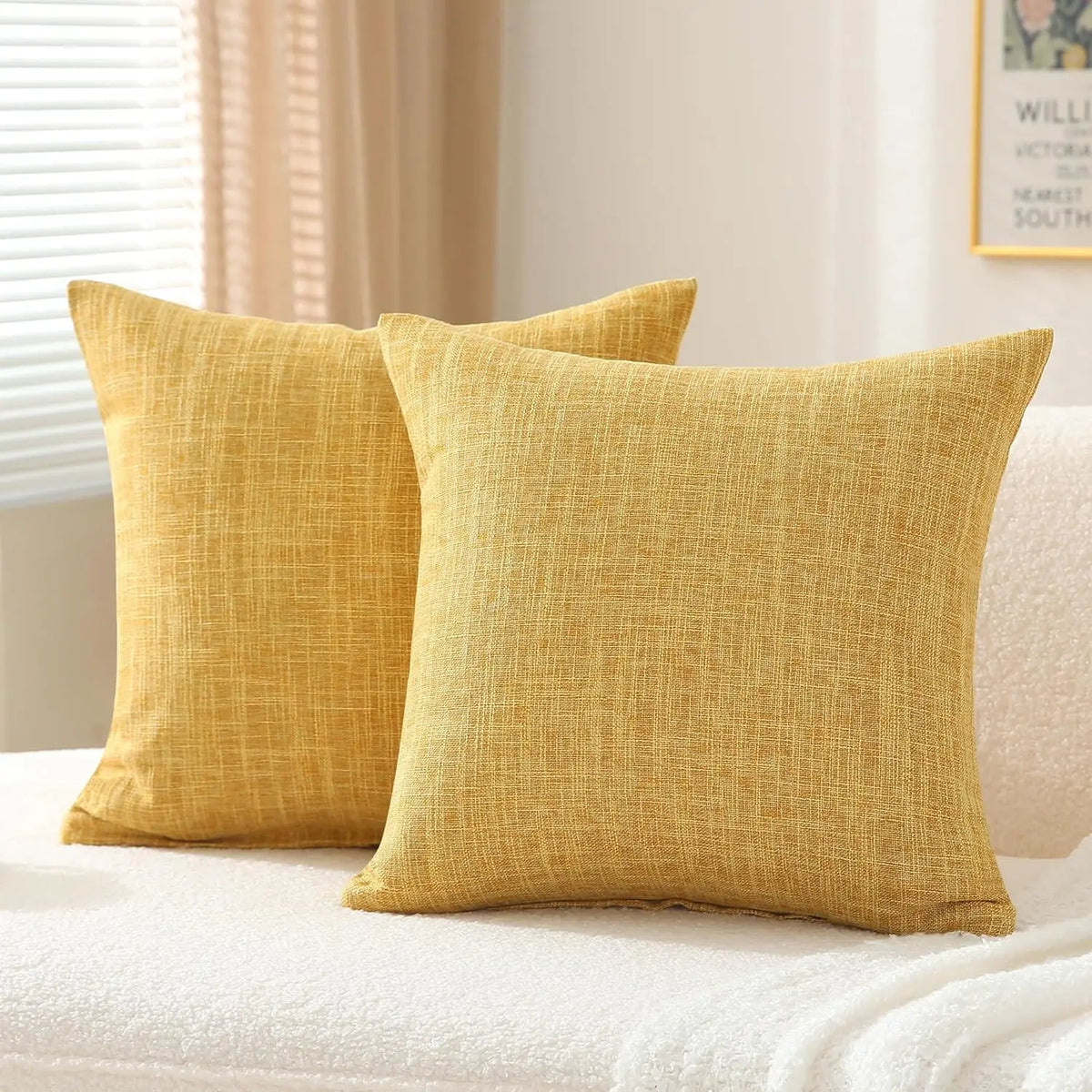 A set of two solid yellow linen pillows resting on a white bed with natural light.
