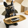 A black bulldog figurine wearing gold-rimmed sunglasses sitting on a brass tray.