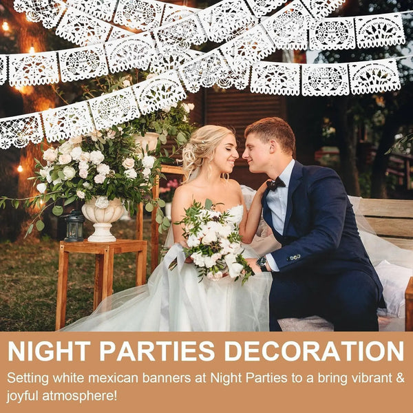 A bride and groom pose in a garden setting decorated with white Mexican fiesta banners for a night party.