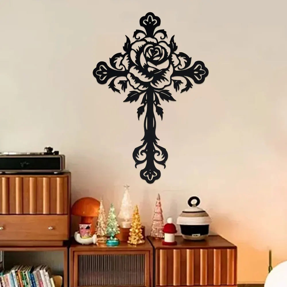 Black decorative metal rose cross wall art hanging on a white wall above wooden furniture.
