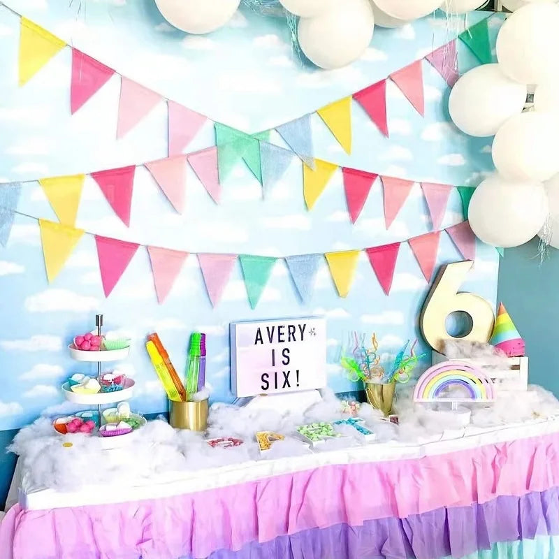 A decoration setup featuring a light blue sky backdrop with colorful pennant banners and white balloons for a party theme.