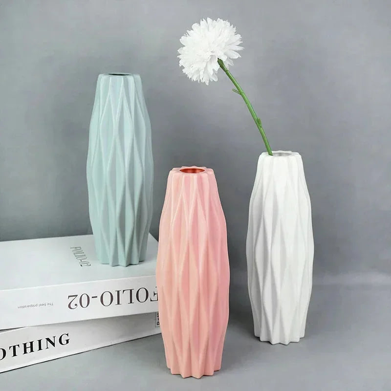 Three tall decorative plastic vases in mint green, pink, and white with a white flower stem.